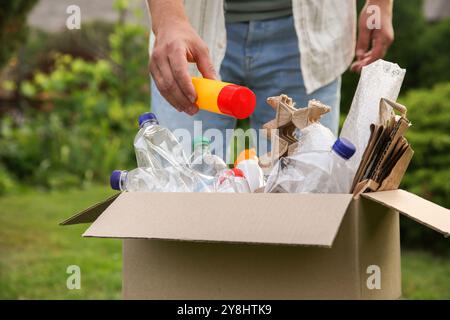 Recyclingkonzept. Mann, der Plastikflasche draußen in Pappkarton steckt, Nahaufnahme Stockfoto