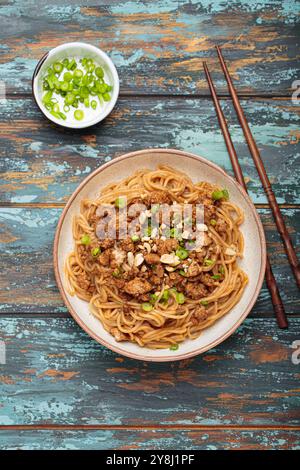 Dan Dan Dan Nudeln serviert mit Essstäbchen und grünen Zwiebeln von oben auf rustikalem Holztisch, traditionelles chinesisches Sichuan-Gericht Stockfoto