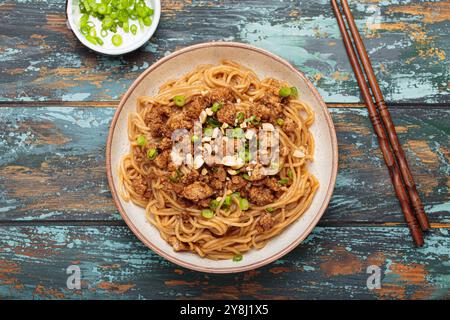 Dan Dan Dan Nudeln serviert mit Essstäbchen und grünen Zwiebeln von oben auf rustikalem Holztisch, traditionelles chinesisches Sichuan-Gericht Stockfoto