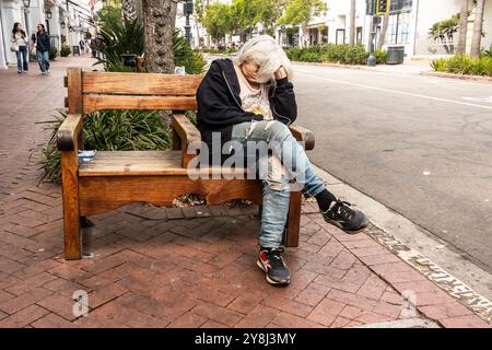 Eine grauhaarige ältere obdachlose Frau schläft auf einer Stadtbank in der State Street in Santa Barbara, Kalifornien. Stockfoto