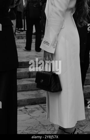 Eine Einladung mit einem langen weißen klassischen Mantel und einer kleinen Clutch-Handtasche in Schwarz von Chanel auf der Elie Saab Show für die Paris Fashion Week SS25 Stockfoto