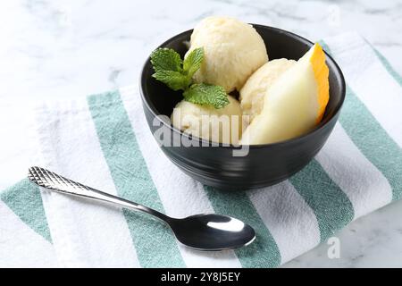 Löffel leckeres Melonensorbet mit Minze in einer Schüssel und Löffel auf weißem Tisch Stockfoto