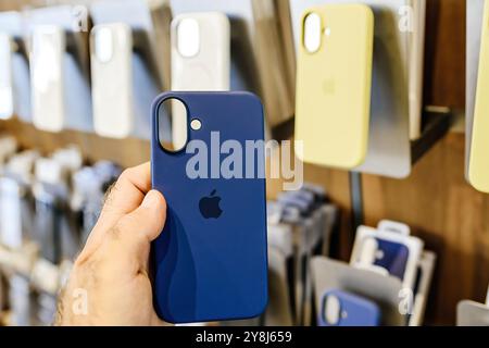 Paris, Frankreich - 20. September 2024: Männliche Hand hält blaue Silikonhülle für iPhone 16 mit mehreren Hüllen im Hintergrund, in einem Apple Store Stockfoto