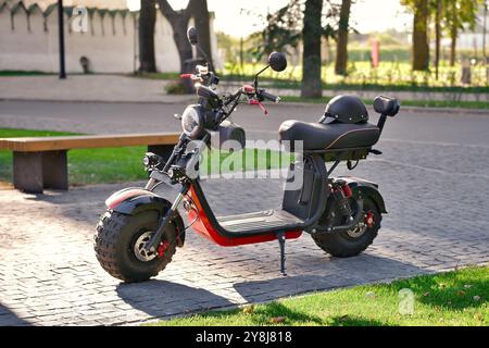 Moderner roter Elektroroller mit Helm auf dem Sitz in der Stadt. Leistungsstarker Elektroroller geparkt. Stockfoto