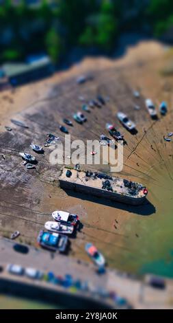 Blick aus der Vogelperspektive auf einen Strand mit Booten am Ufer. Die Szene zeigt verschiedene Boote, die bei Ebbe auf dem Sand geparkt sind, wobei einige Leute herumlaufen. Die Stockfoto