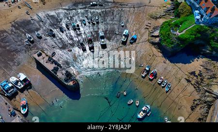 Blick aus der Vogelperspektive auf einen Hafen bei Ebbe mit zahlreichen Booten, die auf dem freiliegenden Schlamm ruhen. Das Wasser ist ruhig mit einer Mischung aus Blau- und Grüntönen, und Th Stockfoto