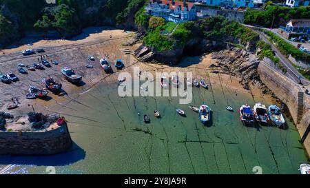 Blick aus der Vogelperspektive auf einen Küstenhafen mit verschiedenen Booten, die bei Ebbe vor Anker liegen. Der Sandstrand ist freigelegt und zeigt Muster im Sand. Umliegende Klippen Stockfoto