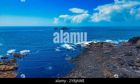 Ein atemberaubender Blick auf die Küste mit einer felsigen Küste und klarem blauem Meer. Der Horizont zeigt einige kleine Inseln und einen hellblauen Himmel mit Stockfoto