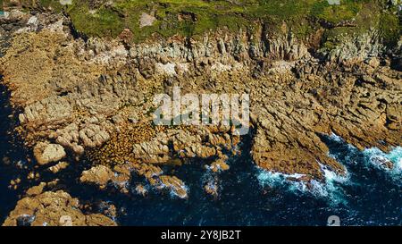 Aus der Vogelperspektive auf die felsige Küste mit klarem blauem Wasser, das gegen die Küste stürzt. Die Landschaft bietet zerklüftete Klippen und verstreute Felsbrocken, Showcasi Stockfoto