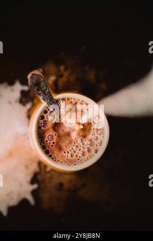 Blick von oben auf eine Tasse heißen, duftenden Kaffee mit kalter Milch. Der Prozess der Zubereitung eines köstlichen Getränks für den Morgen. Unordentlich. Stockfoto