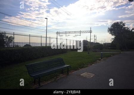 Pfad in einem Park neben einem Schutzzaun einer Eisenbahn am Meer bei Sonnenuntergang Stockfoto