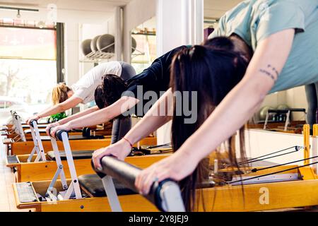 Gruppe junger Frauen, die auf dem Pilates-Bett der Reformatoren trainieren. Stockfoto
