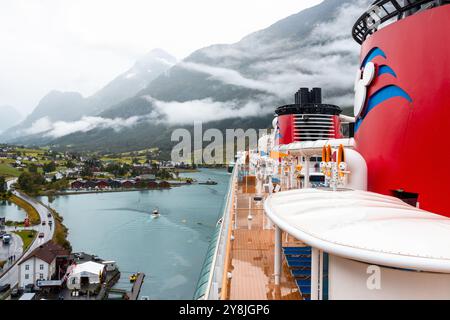 Disney Kreuzfahrtschiff 15. August 2024 - das Schiff liegt im malerischen Fjord von Olden, Norwegen. Rote Schornsteine und das Mickey-Maus-Emblem sind sichtbar Stockfoto