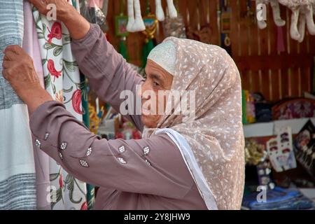 Chiwa, Usbekistan; 21. September 2024: Eine ältere usbekische Frau, die an ihrem Textilstand auf den Basaren von Chiwa, Usbekistan, arbeitet. Traditionell gekleidet im AT Stockfoto