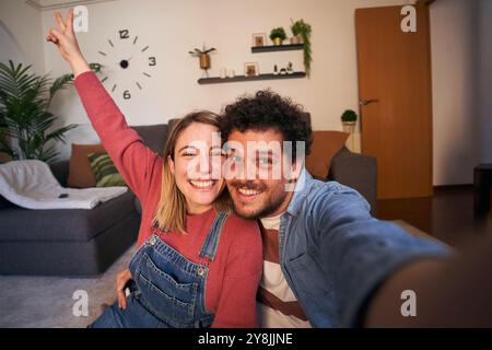 Fröhliches, junges, weißes Paar, das Selfie macht und zu Hause lächelnd in die Kamera blickt. Fröhliche Leute Stockfoto
