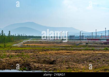 Eine abgelegene Baustelle mit einer unbefestigten Straße, die in die Ferne führt, umgeben von Vegetation und Bergen. Bedeckter Himmel und entfernte Stromleitungen cr Stockfoto