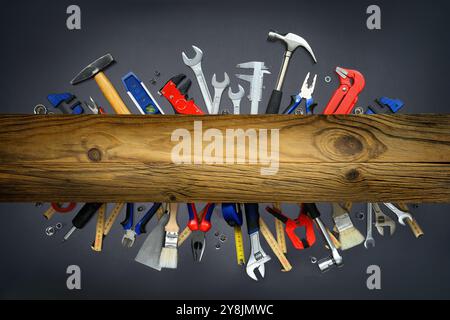 Ein Satz Werkzeuge auf grauem Hintergrund mit einer Holzdiele oben in einer auffälligen Anordnung. Das elegante Holz in der Mitte kann als Kopierraum genutzt werden Stockfoto