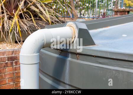 Foto: Leitung aus Polyvinylchlorid (PVC), die über eine Winkelverbindung mit einem großen Kunststoff-Wassertank im Freien verbunden ist. Der Tank ist eine statische Wasserversorgung für Stockfoto
