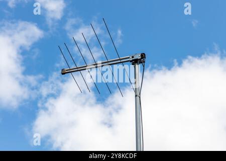 Foto einer traditionellen Fernsehantenne auf dem Dach eines Wohnhauses vor einem blauen Himmel mit weißen Wolken im Hintergrund. Stockfoto