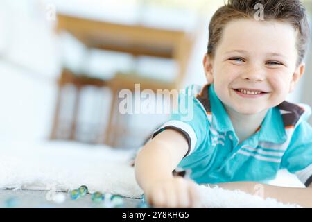 Glückliches Kind, Porträt und Kind spielen mit Marmor auf dem Boden zum Spielen, Entspannen und Spaß zu Hause. Lächeln, Gesicht und Junge mit Glaskugeln oder Spielzeug auf dem Boden für c Stockfoto