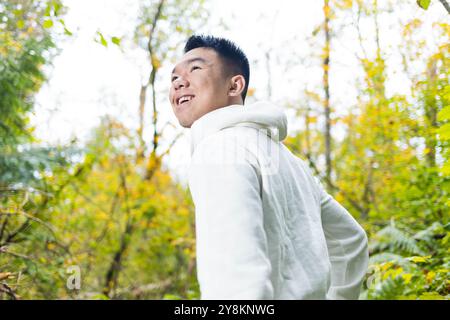 Ein junger männlicher Teenager macht einen Spaziergang durch den Wald und blickt zurück, um die umliegende Natur im Herbst zu schätzen Stockfoto