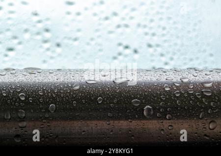 Seitenansicht von Regentropfen, die Muster auf einer glatten Oberfläche aus Metall bilden. Textur für frischen Regen. Stockfoto