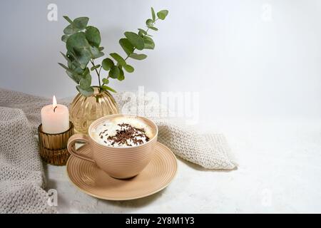 Tasse heiße Schokolade oder Cappuccino mit Schlagsahne, Kerze und einer Vase mit Zweigen, süßes Getränk für kalte Tage in einem gemütlichen Zuhause, heller Hintergrund, Kopie Stockfoto