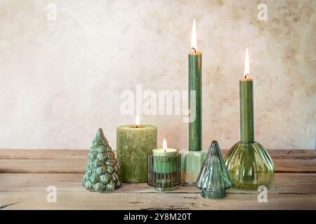 Vier verschiedene grüne Kerzen und einfache Weihnachtsdekoration aus Glas und Keramik auf rustikalem Holzbrett, minimales Adventsarrangement, hell B Stockfoto