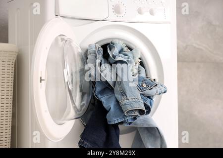 Waschmaschine mit schmutzigen Jeans und anderen Denim-Kleidern im Innenbereich Stockfoto