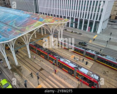 Moderne Straßenbahnhaltestelle in Łódź, Polen, mit lebhaften Straßenbahnen und farbenfrohem Dachdach in einer geschäftigen städtischen Umgebung an einem bewölkten Tag Stockfoto