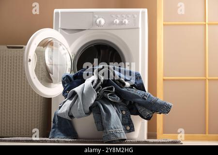 Waschmaschine mit schmutzigen Jeans und anderen Denim-Kleidern im Innenbereich Stockfoto