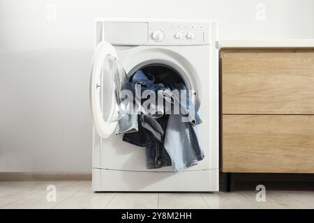 Waschmaschine mit schmutzigen Jeans und anderen Denim-Kleidern im Innenbereich Stockfoto