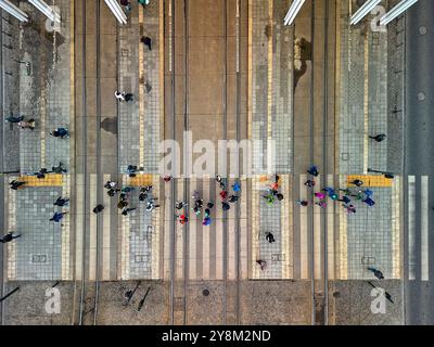 Top-Down-Ansicht von Fußgängern, die Straßenbahnschienen überqueren, in einer geschäftigen städtischen Umgebung in Łódź, Polen, von oben mit geometrischen Mustern von Bürgersteigen und Stockfoto