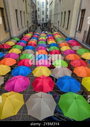 Lebendige Overhead-Ausstellung mit mehrfarbigen Regenschirmen, die zwischen zwei Gebäuden in einem schmalen Innenhof in Łódź, Polen, hängen Stockfoto