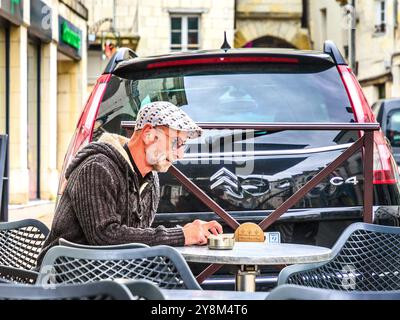 Mann in Stoffmütze saß am Außencafé-Tisch und prüfte Smartphone - Loches, Indre-et-Loire (37), Frankreich. Stockfoto