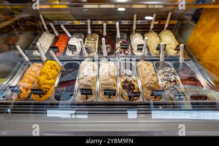 Eis mit verschiedenen Geschmacksrichtungen in Edelstahlblechen in der Kühltheke der italienischen Eismaschine mit Geschmacksbezeichnungen Stockfoto