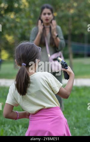 Ein kleines Mädchen mit Pistole terrorisiert ihre Mutter. Der Begriff der Gefahr von Waffen in Reichweite von Kindern Stockfoto