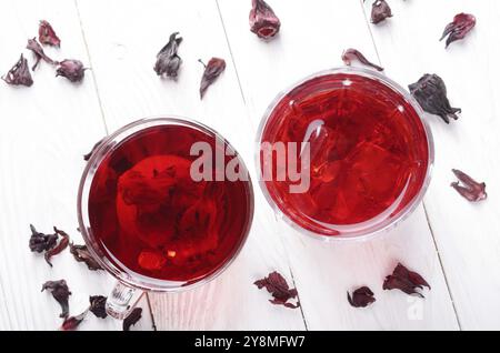 Draufsicht bei zwei Tassen mit Eis und trockenen Hibiscus Blüten auf Weiß Holztisch Hintergrund Stockfoto