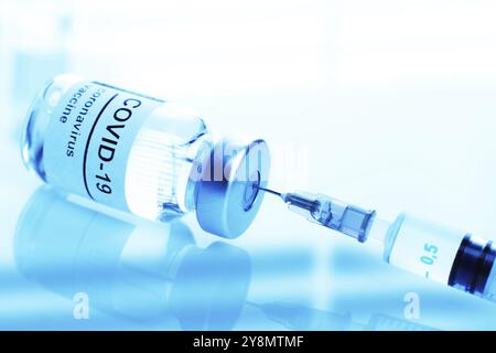 Blaues Fläschchen aus getöntem Glas mit Etikett für Coronavirus-Impfstoff und Nahaufnahme der Spritze Stockfoto