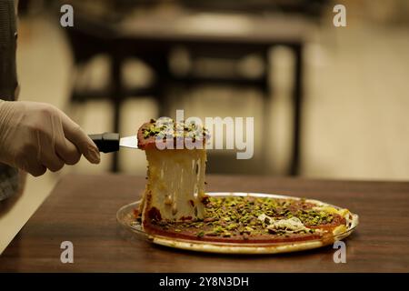 Gaziantep, Türkei. Kanafeh ist ein Dessert aus dem Nahen Osten, das aus Grießteig und dünnem, geriebenem Gebäck besteht, das in einem einfachen süßen Sirup eingeweicht wird. Diese Art von Kanafeh soll palästinensischer Herkunft sein, insbesondere aus der Stadt Nablus, und verbreitete sich dann unter anderen Levantenländern wie Syrien. Die jüngste Einwanderung von Syrern in Nachbarländer, in denen Syrer ihre Fertigkeiten in der Konditorei erworben haben, hat den Weg zur Popularität geebnet Stockfoto