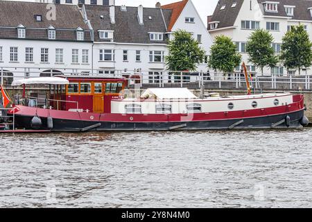 Rotes Schiff ankerte am Ufer der Promenade entlang des Flusses Maas, Häuser mit weißen Wänden im Hintergrund, Stadtbild der Stadt Maastricht in Süd-Limburg, ne Stockfoto