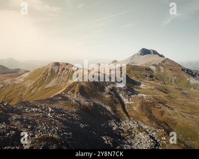 Drohnenblick auf die Savognin Berge in der Schweiz bei Sonnenuntergang mit Blick auf zerklüftete Gipfel und Täler, die in goldenes Licht getaucht sind Stockfoto