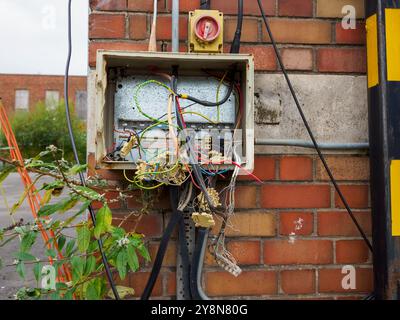 Freiliegende und verwickelte elektrische Leitungen in einem Versorgungskasten im Freien an einer Ziegelwand. Stockfoto