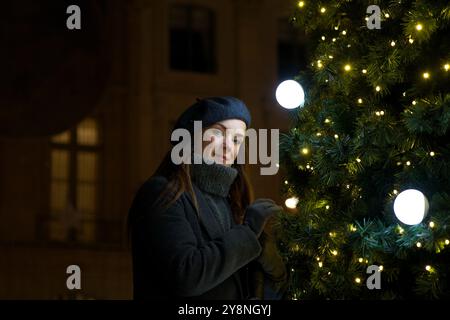 Die Pariser Frau im grauen Mantel bewundert das Neujahrsspielzeug am Weihnachtsbaum Stockfoto