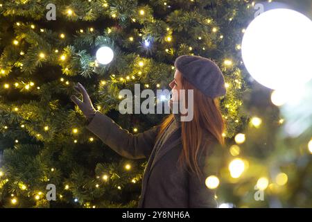 Pariser Frau im grauen Mantel, die Neujahrsdekorationen am Weihnachtsbaum bewundert Stockfoto