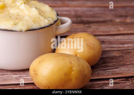 In einer gemütlichen Atmosphäre werden auf einem alten Holztisch neben ganzen Kartoffeln geschlagene Kartoffelpüree geschenkt, die Thanksgiving-Essenzen einfangen Stockfoto