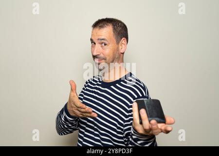 Bärtiger hispanischer Mann in seinen 40ern, der glücklich und stolz seinen Geldbeutel voller Geld anbietet, isoliert über beigefarbenem Hintergrund. Stockfoto