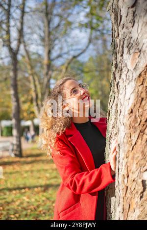 Fröhliche junge Frau mit Brille steht an einem Baum im Park *** fröhliche junge Frau mit Brille steht an einem Baum im Park Stockfoto