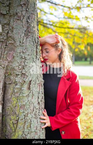 Nachdenkliche junge Frau mit Brille steht an einem Baum im herbstlichen Park *** nachdenkliche junge Frau mit Brille steht an einem Baum in einem herbstlichen Park Stockfoto