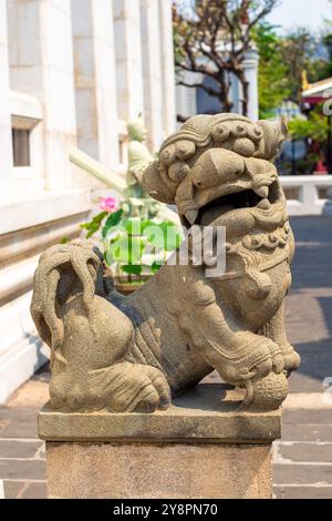 Steinfigur eines chinesischen Löwen am Fuße eines buddhistischen Tempels in Asien. Statue am Bowonniwetin Tempel. Stockfoto